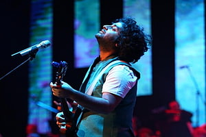 Arijit Singh performing passionately on stage with guitar under dramatic blue lighting HD wallpaper