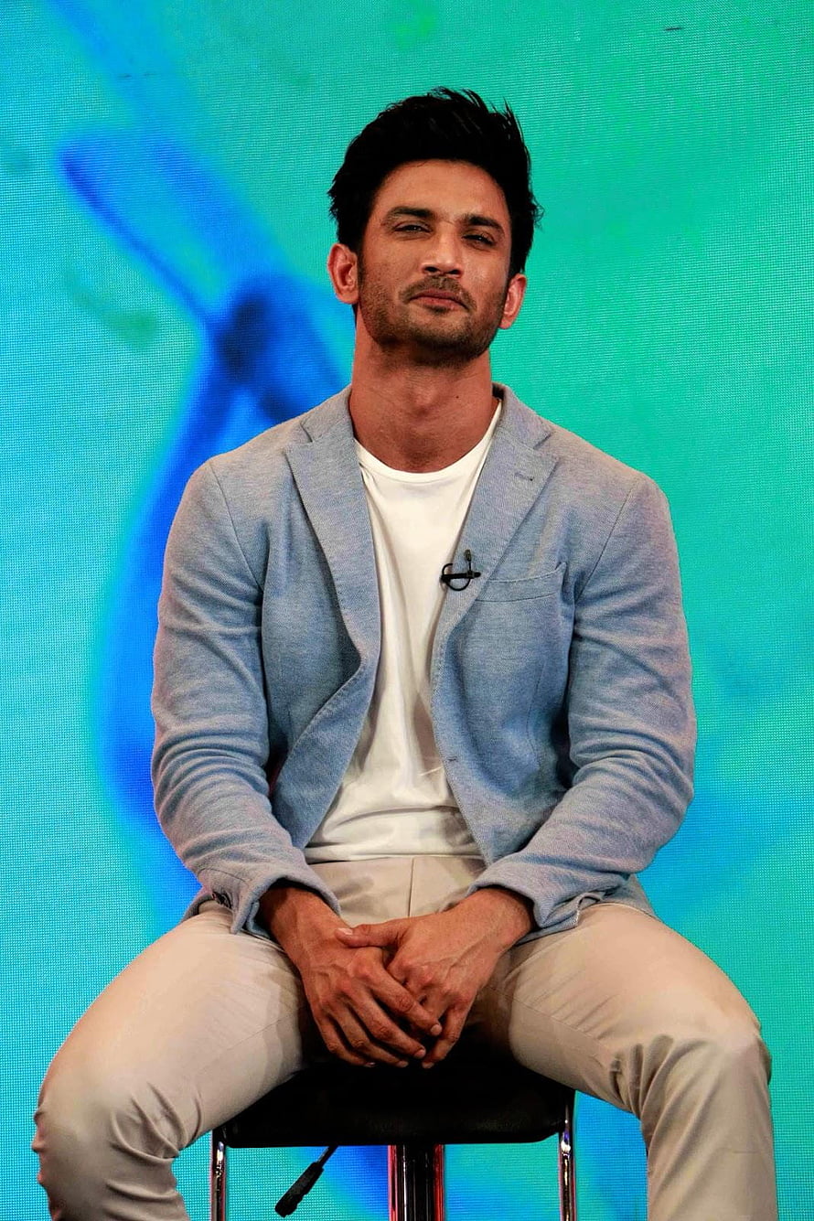 Sushant Singh Rajput in a light blue blazer and white t-shirt seated on a stool against a teal backdrop HD phone wallpaper