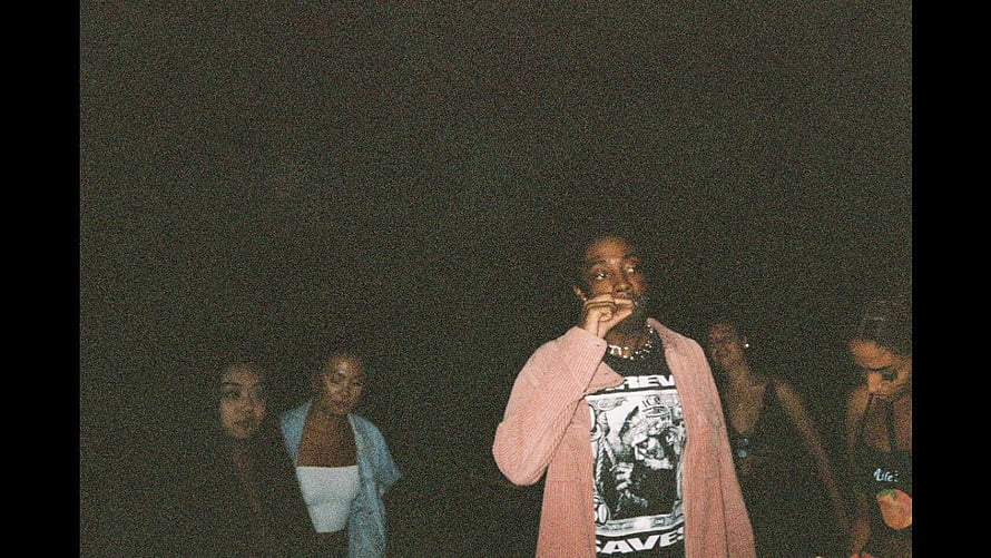 Brent Faiyaz in a pink cardigan with friends in a dark grainy night scene HD wallpaper
