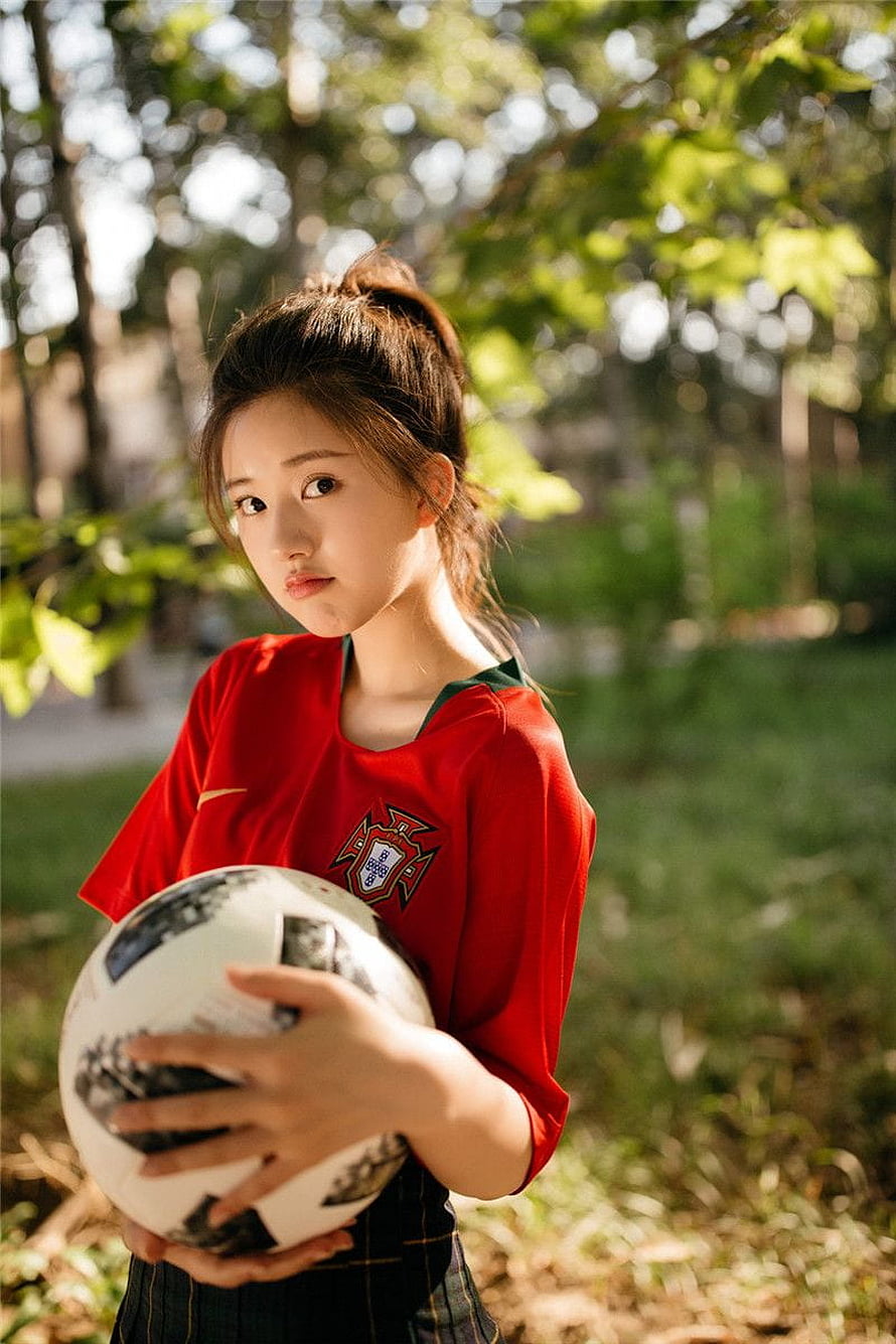 Zhao Lusi in a red Portugal football jersey holding a soccer ball in a sunlit park HD phone wallpaper