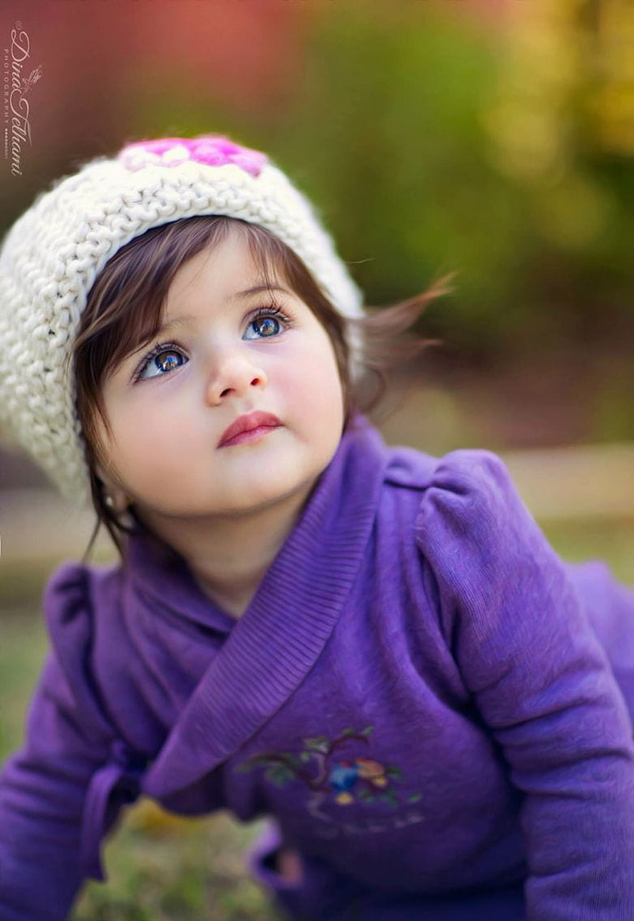 Adorable baby girl in a purple wrap dress and white knit hat gazing upward outdoors HD phone wallpaper