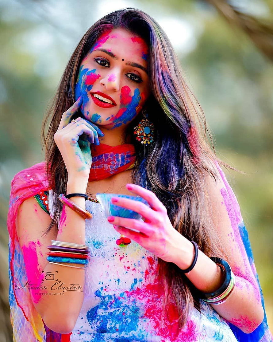 Smiling woman with vibrant Holi colors on face and hands holding a small bowl HD phone wallpaper