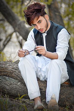 Young man in white kurta and black waistcoat sitting on a tree trunk holding glasses HD phone wallpaper