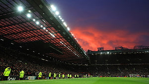 Old Trafford Stadium at Dusk with Dramatic Red Sky and Floodlights HD wallpaper