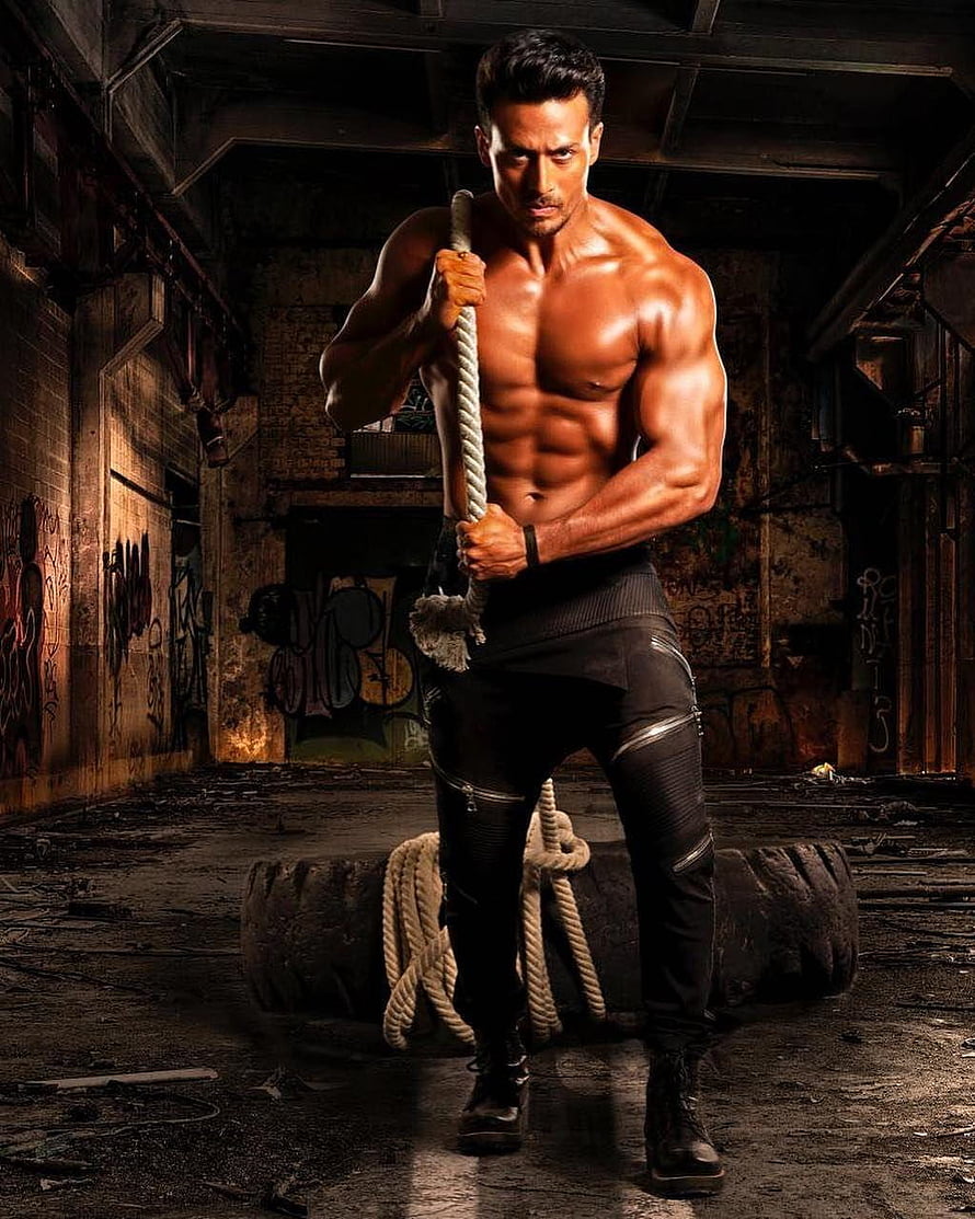 Tiger Shroff in a gritty urban gym setting, shirtless and gripping a thick rope with intense focus HD phone wallpaper