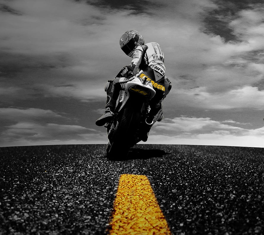 Rider on a Yamaha racing motorcycle leaning into a turn on an open asphalt road under a dramatic cloudy sky HD wallpaper