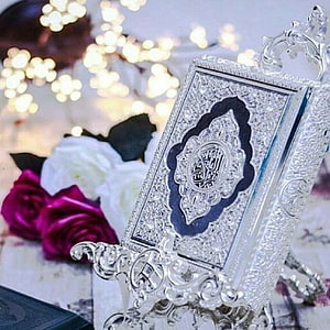 Ornate Silver Quran Stand with Intricate Engraving and Floral Arrangement HD phone wallpaper