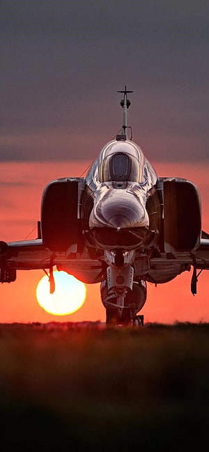 F-4 Phantom II fighter jet front view silhouetted against a dramatic sunset sky HD phone wallpaper