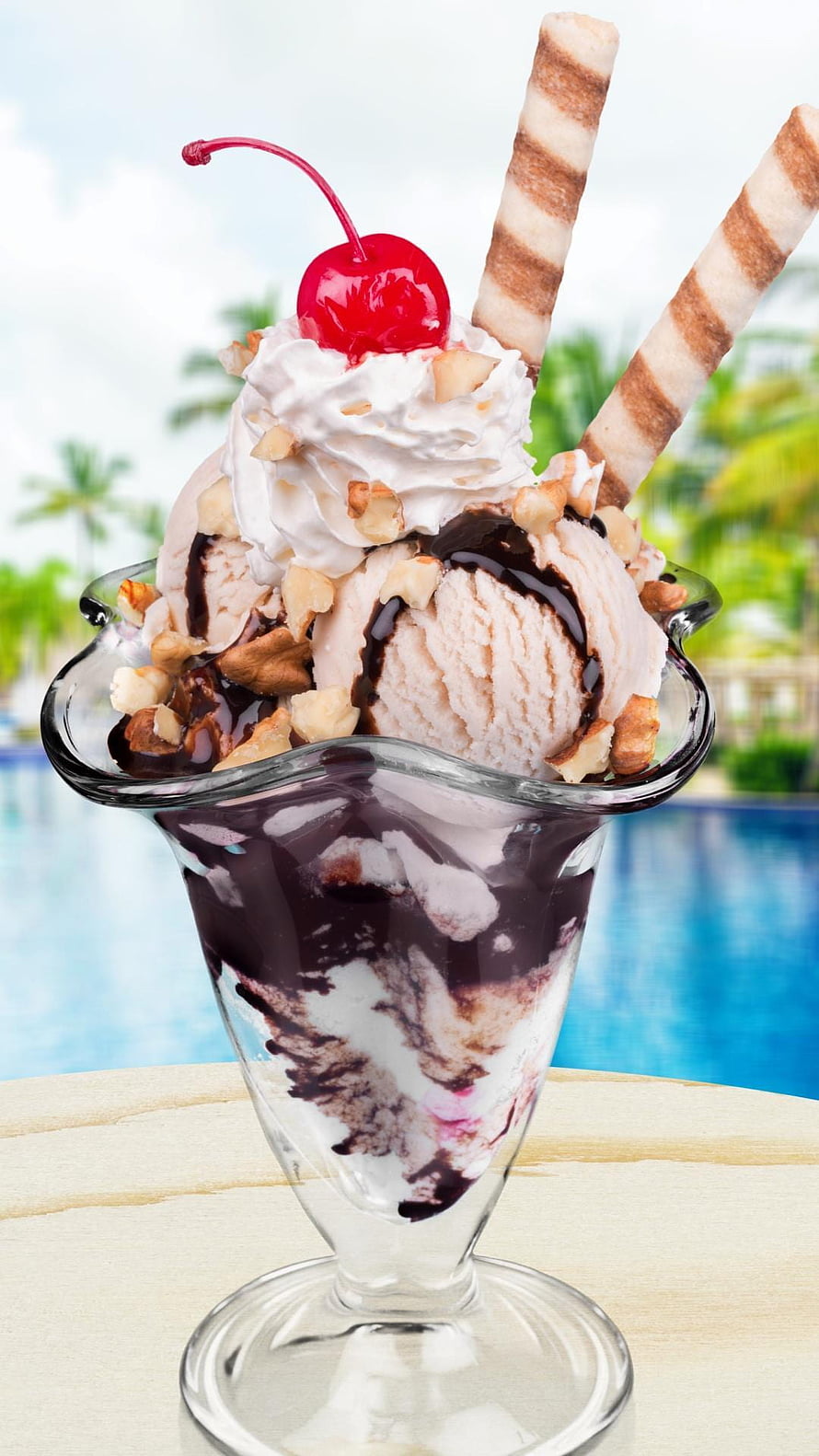Classic Sundae with Chocolate Sauce, Whipped Cream, and Cherry on a Tropical Poolside Background HD phone wallpaper