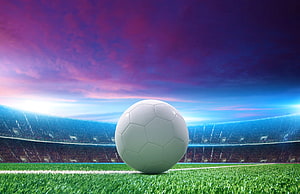 Soccer Ball on Green Pitch in a Large Stadium Under a Vibrant Sunset Sky HD wallpaper