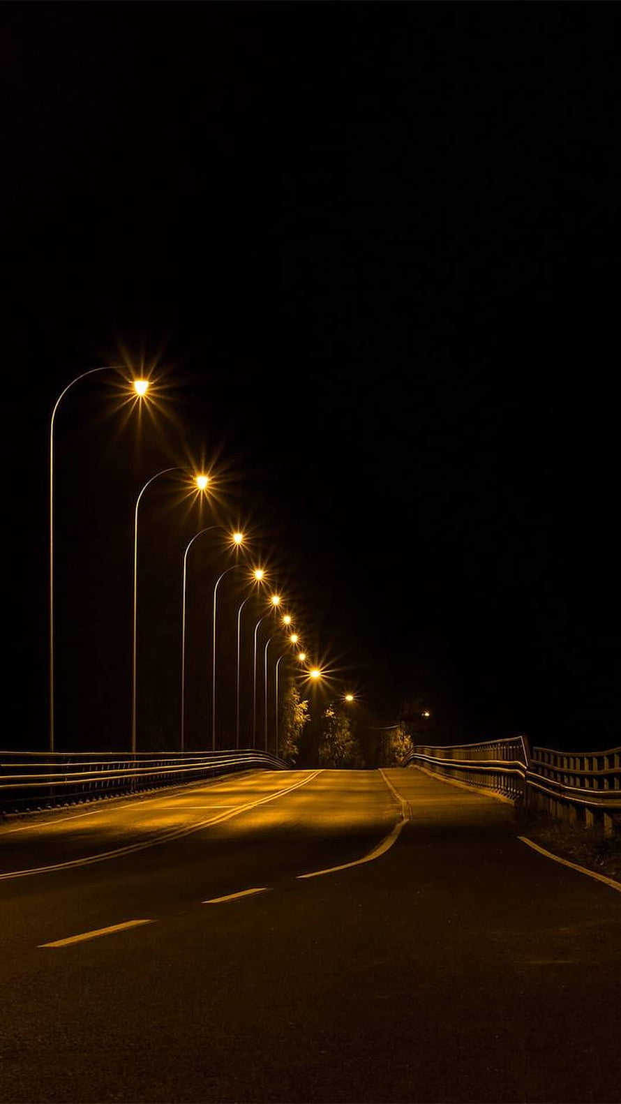 Empty Highway at Night Illuminated by a Row of Warm Street Lamps HD phone wallpaper