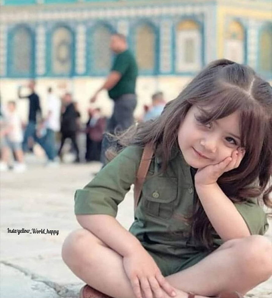 Cute Young Girl Sitting Cross-Legged in Green Outfit with Soft Smile HD phone wallpaper