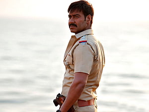 Ajay Devgan as Inspector Singham in khaki police uniform standing by the sea HD wallpaper