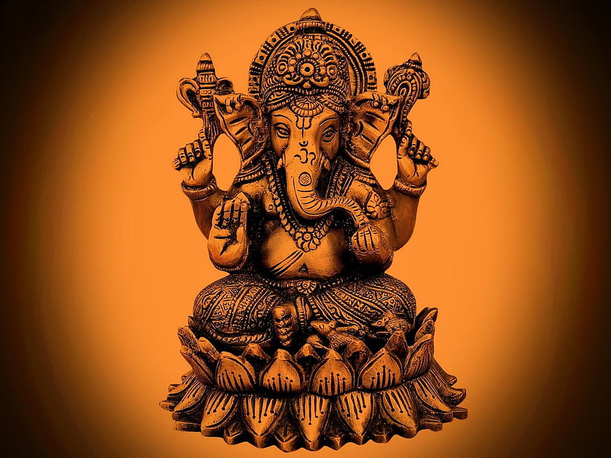 Ganesha seated on a lotus throne with four arms and ornate crown in warm golden tones HD wallpaper