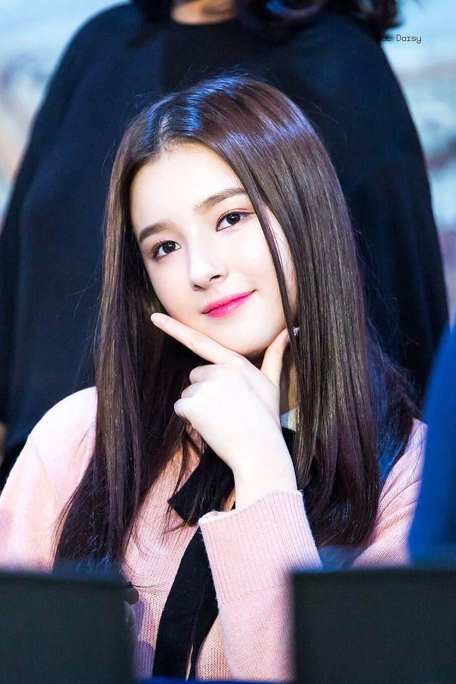 Momoland Nancy in a soft pink sweater with a gentle smile and finger on chin HD phone wallpaper