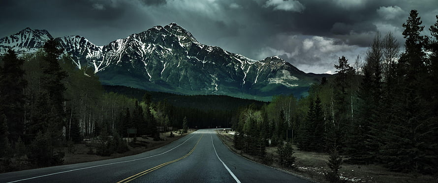 Moody Mountain Road Through Pine Forest Under Stormy Skies HD wallpaper