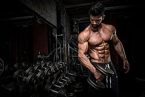 Sergi Constance Performing Dumbbell Curl in Dark Industrial Gym Setting HD wallpaper
