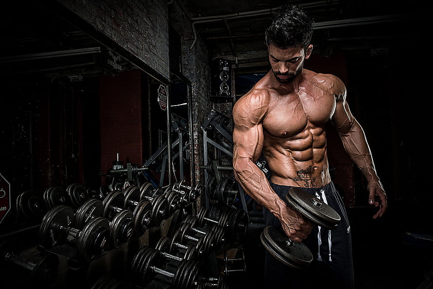 Sergi Constance Performing Dumbbell Curl in Dark Industrial Gym Setting HD wallpaper