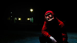 Person in red hoodie wearing a glowing LED mask with X eyes in a dark night setting HD wallpaper