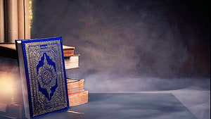 Blue Quran Book with Gold Embossing on Stack of Ancient Volumes in Misty Atmosphere HD wallpaper