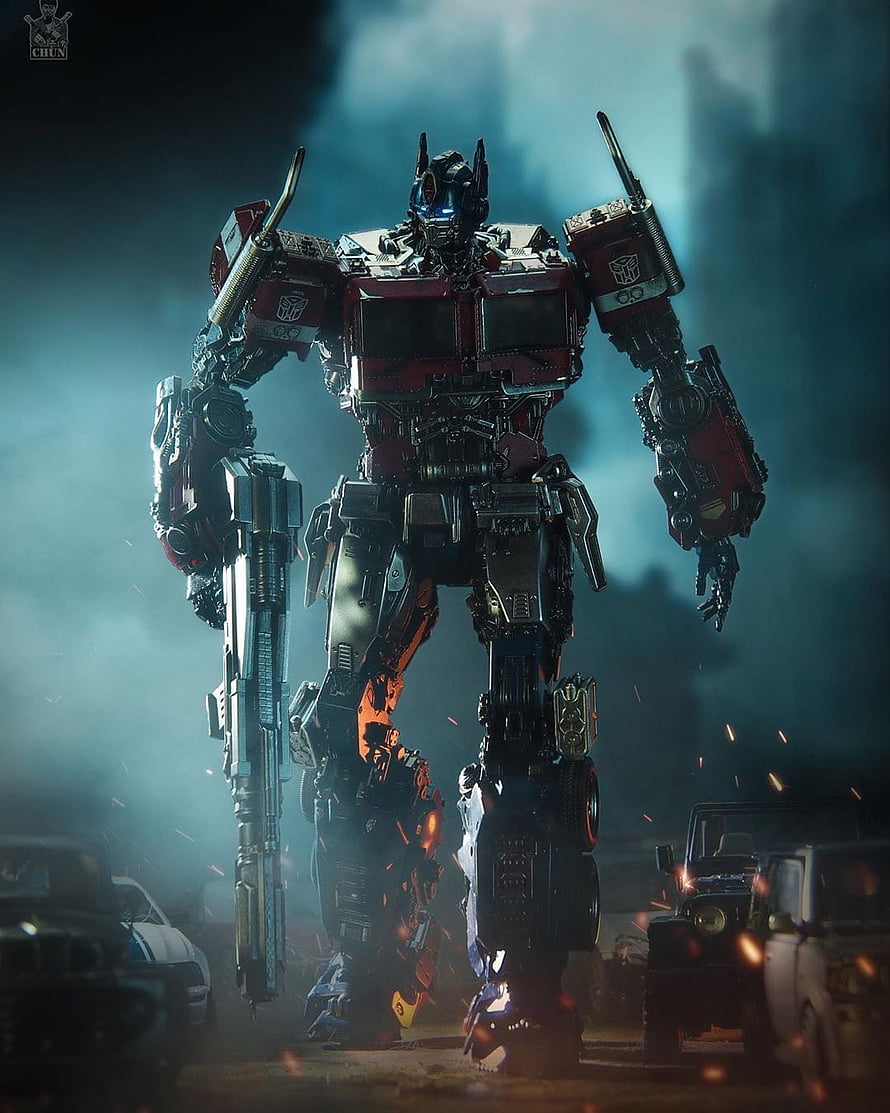 Optimus Prime Standing in a Smoky Battlefield with Wrecked Vehicles and Flying Embers HD phone wallpaper