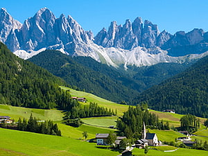 Alpine Village with Church Nestled in Green Pastures Beneath Dramatic Dolomite Peaks HD wallpaper