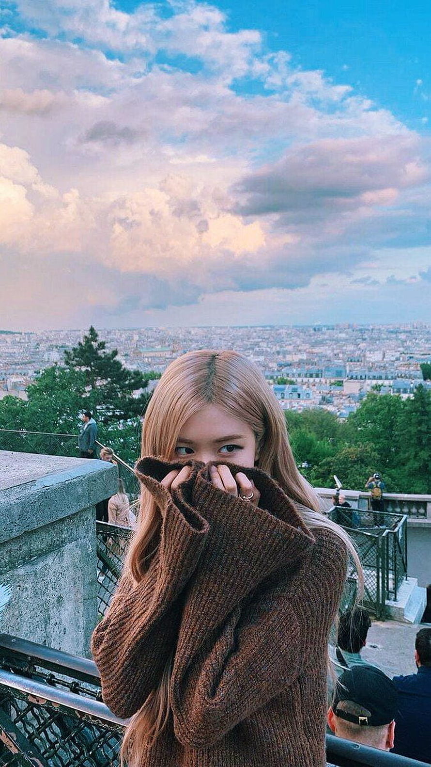 Rosé from Blackpink in a brown knit sweater overlooking the Paris cityscape under a dramatic cloudy sky HD phone wallpaper