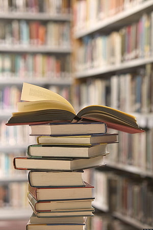 Open book resting on a tall stack of hardcovers in a library aisle HD phone wallpaper