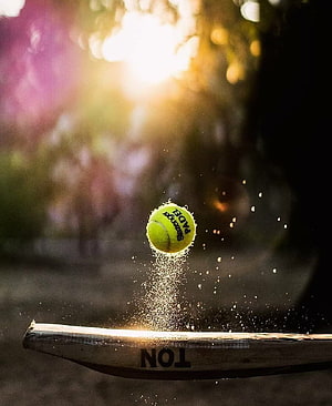 Paddle ball striking a wooden bat with dust particles in golden sunlight HD phone wallpaper