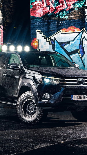 Black Toyota Hilux Pickup Truck with Off-Road Tires Parked Against Vibrant Street Art Mural HD phone wallpaper