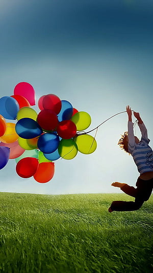 Child Leaping in Green Meadow Holding a Large Bunch of Colorful Balloons HD phone wallpaper