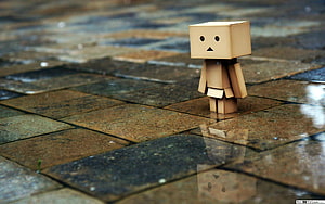 Lonely cardboard robot figure standing on wet stone pavement with reflection HD wallpaper