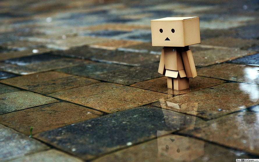 Lonely cardboard robot figure standing on wet stone pavement with reflection HD wallpaper