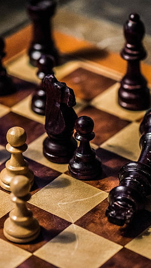 Close-up of wooden chess pieces on a checkered board with dramatic lighting HD phone wallpaper