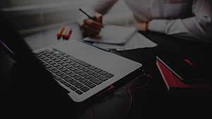 Professional Workspace with Laptop, Notebook, and Red Earbuds on Dark Desk HD wallpaper