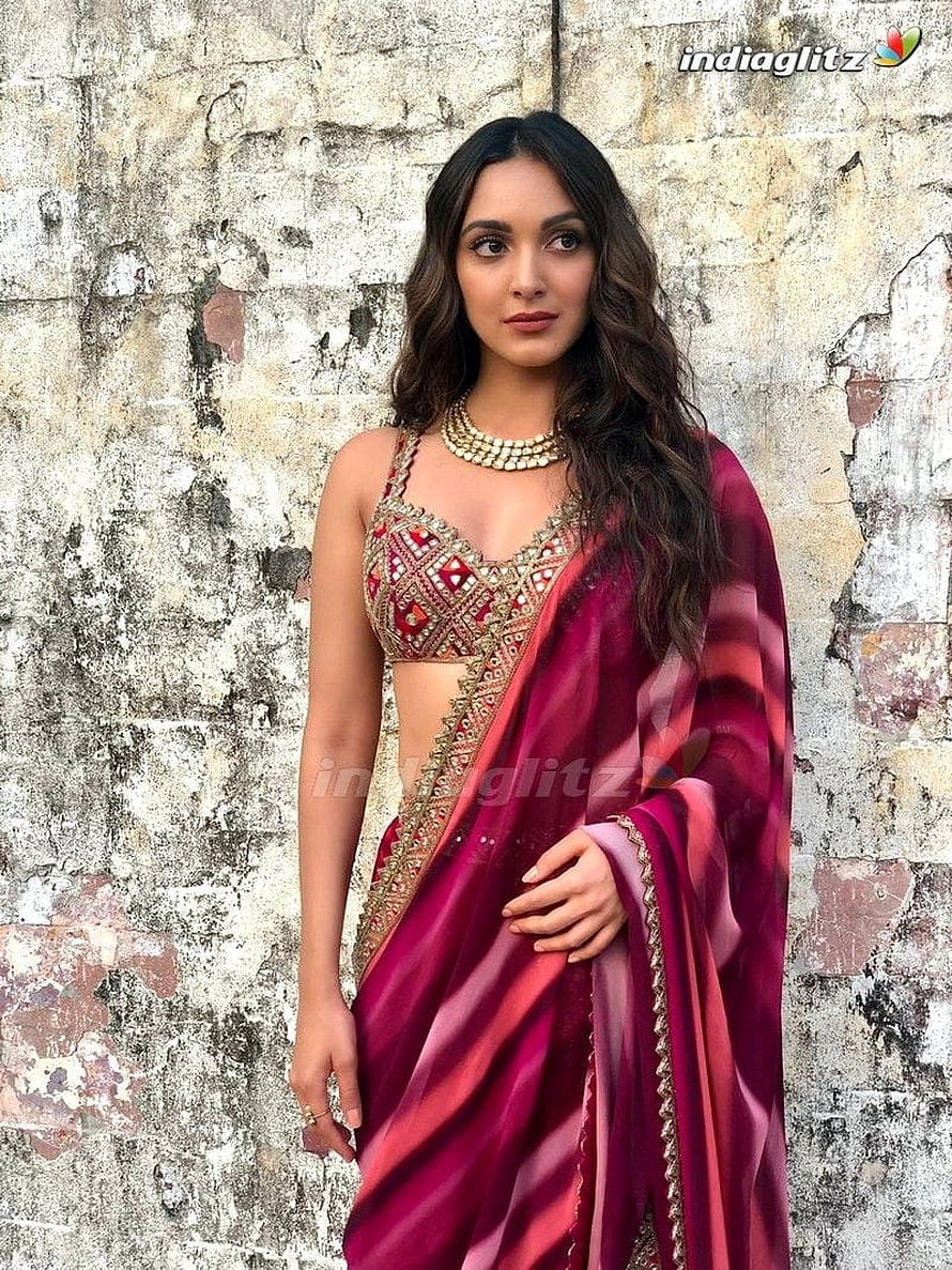 Kiara Advani in a deep magenta silk saree with gold embroidered blouse against a weathered stone wall HD phone wallpaper