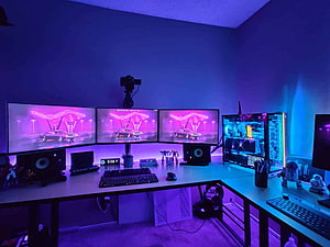 Triple Monitor Gaming Battlestation with RGB PC Tower and Neon Purple Ambient Lighting HD wallpaper