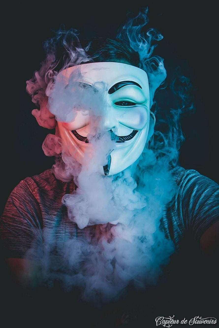 Guy Wearing Guy Fawkes Mask Surrounded by Dramatic Smoke and Neon Lighting HD phone wallpaper