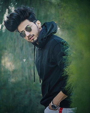 Stylish Young Man in Black Hoodie and Round Sunglasses in a Lush Green Forest HD phone wallpaper