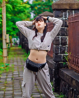 Riva Arora in a beige cropped hoodie and cargo pants with a black fanny pack on a stone pathway HD phone wallpaper