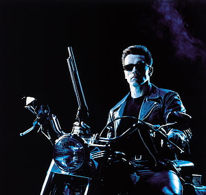 Arnold Schwarzenegger as the Terminator on a motorcycle with a shotgun in a dark cinematic scene HD wallpaper