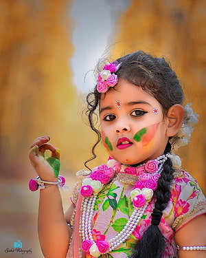 Adorable Little Girl Celebrating Holi Festival With Vibrant Face Paint and Floral Accessories HD phone wallpaper