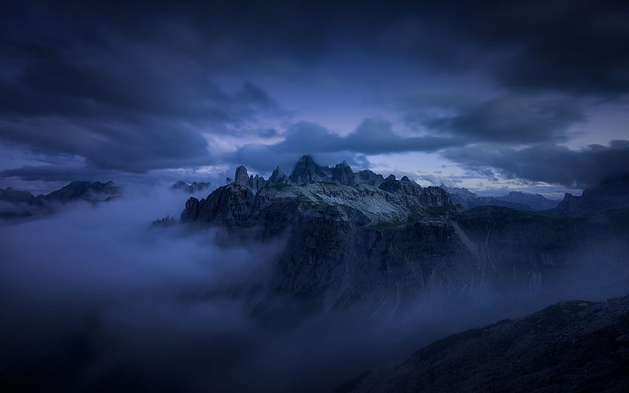 Dramatic Dark Clouds Enveloping Jagged Mountain Peaks in Misty Blue Twilight HD wallpaper