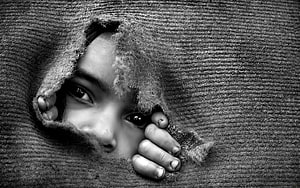 Black and white portrait of a child peering through a torn woolen blanket HD wallpaper