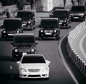Black Mercedes G-Class convoy escorting a white sedan on a curved road HD wallpaper