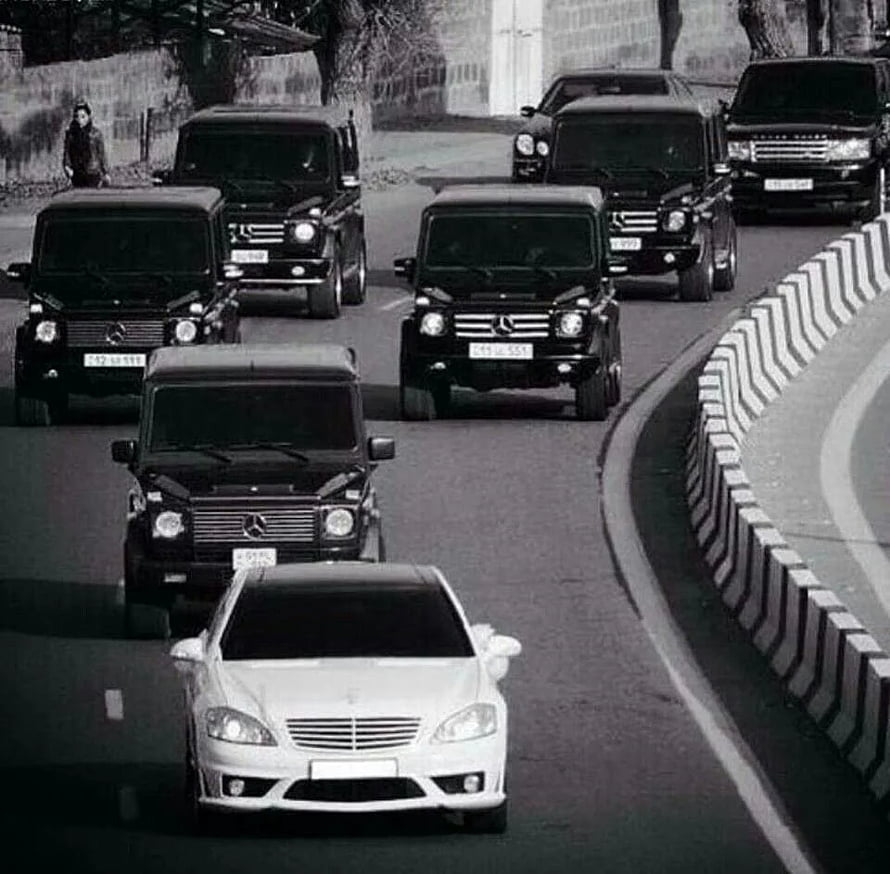 Black Mercedes G-Class convoy escorting a white sedan on a curved road HD wallpaper