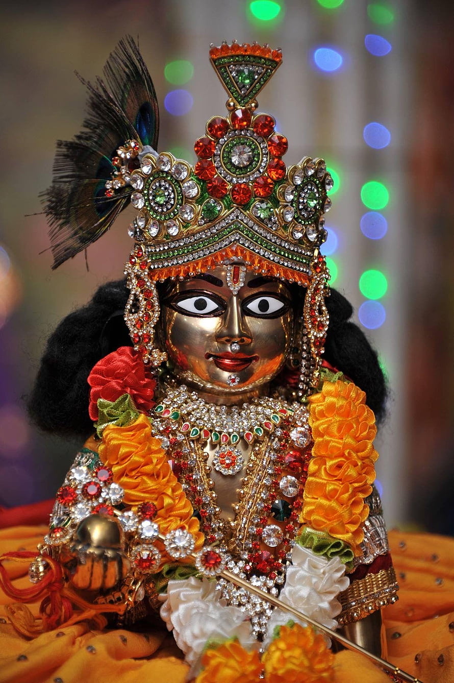 Laddu Gopal ornate deity statue adorned with jeweled crown, marigold garlands, and peacock feather HD phone wallpaper