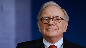 Warren Buffett in a dark suit with a red tie and glasses against a blue background HD wallpaper