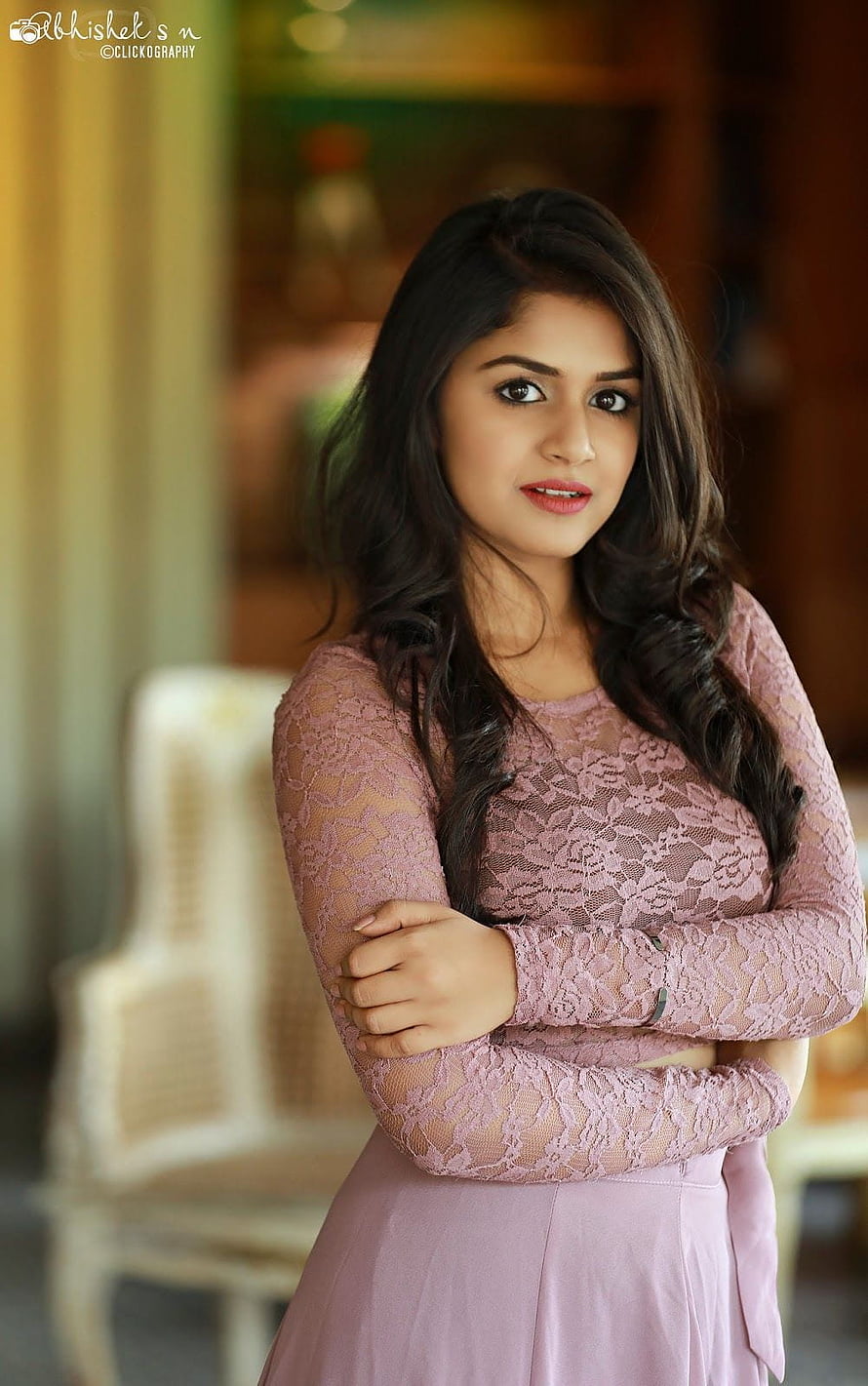 Sanjana Anand in a pink lace top and skirt with arms crossed in a warm indoor setting HD phone wallpaper
