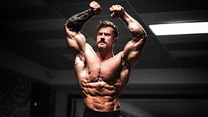 Chris Bumstead Classic Physique Bodybuilding Pose in Dark Gym Setting HD wallpaper